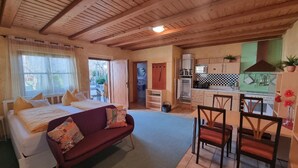 A cozy room with a bed, a sofa, a dining area with chairs, a kitchen with cabinets and appliances, and a view through an open door. - Ferienhäusle Sommerach (Sommerach)