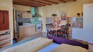 A compact room with a bed, a dining table with chairs, a kitchenette, and a large window. - Ferienhäusle Sommerach (Sommerach)