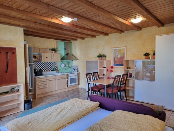 Une pièce compacte comprenant un lit, une table à manger avec des chaises, un coin cuisine et une grande fenêtre.