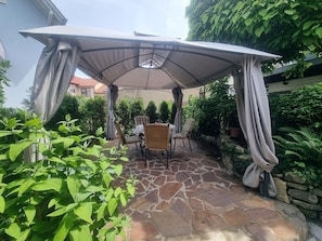 Une terrasse en pierre avec une pergola, des chaises en osier et une table.