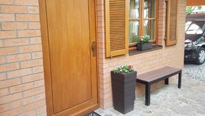 A brick building with a wooden door, two windows with shutters, a bench, and a planter with flowers. - Ferienhäusle Sommerach (Sommerach)