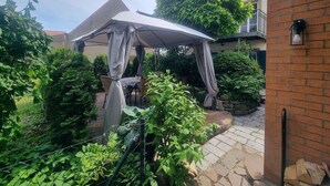 A covered outdoor seating area with a table and chairs, surrounded by greenery and a brick wall. - Ferienhäusle Sommerach (Sommerach)
