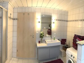 Un baño moderno con ducha, lavabo, espejo y lavadora.