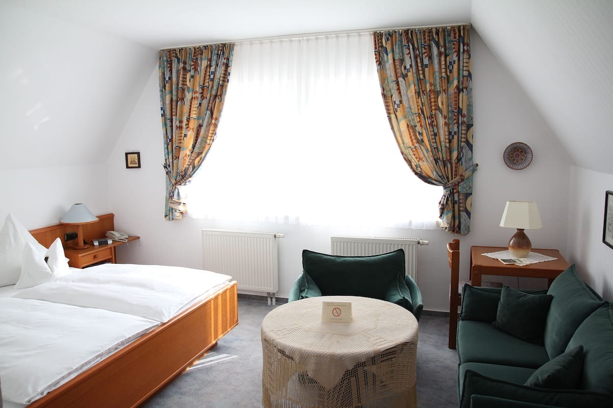 Une chambre d’hôtel avec un lit, une table ronde, un canapé et une fenêtre avec des rideaux.