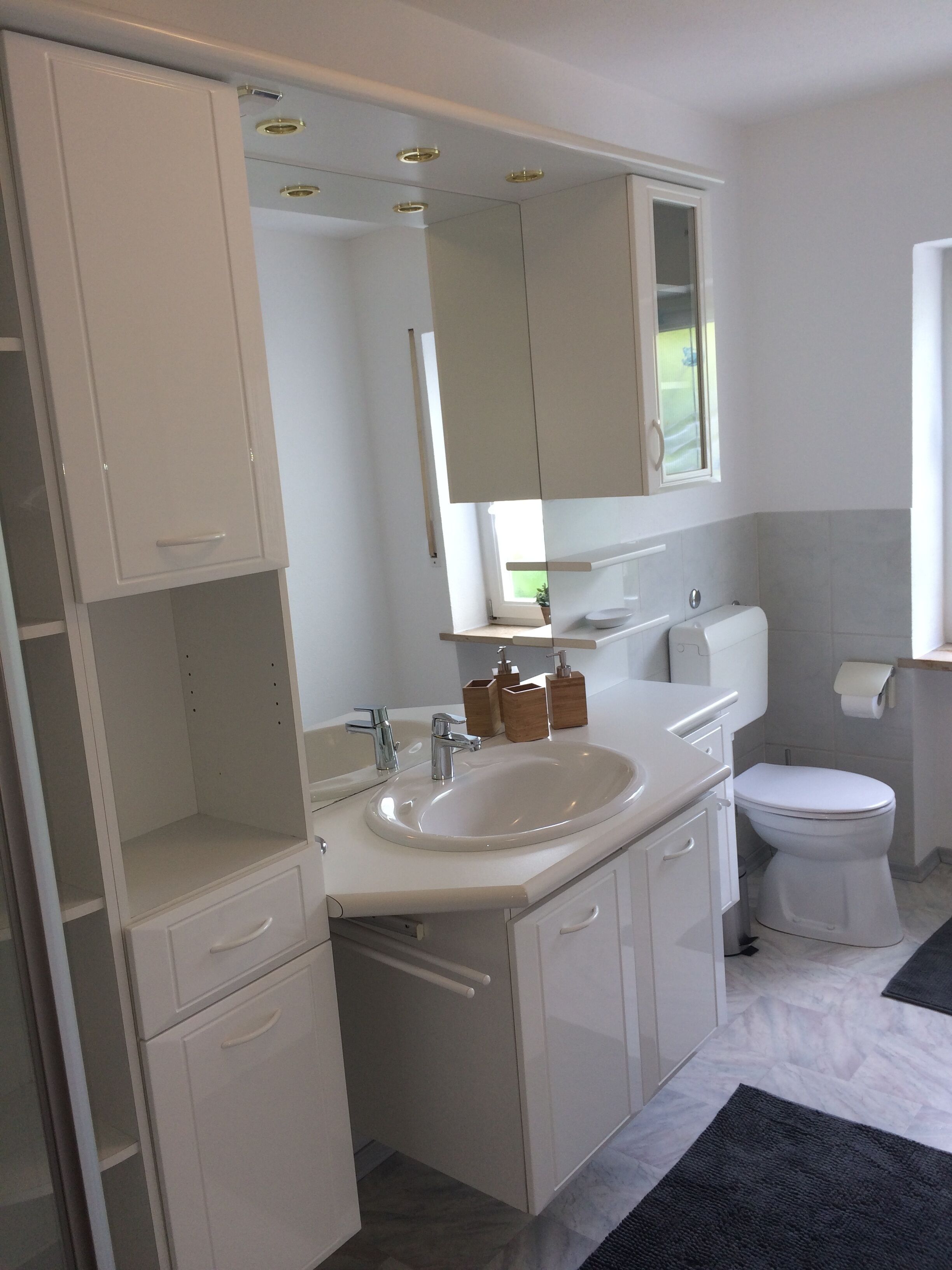 A modern bathroom with a white sink, mirror, and toilet. There are wooden storage boxes and a towel rack.