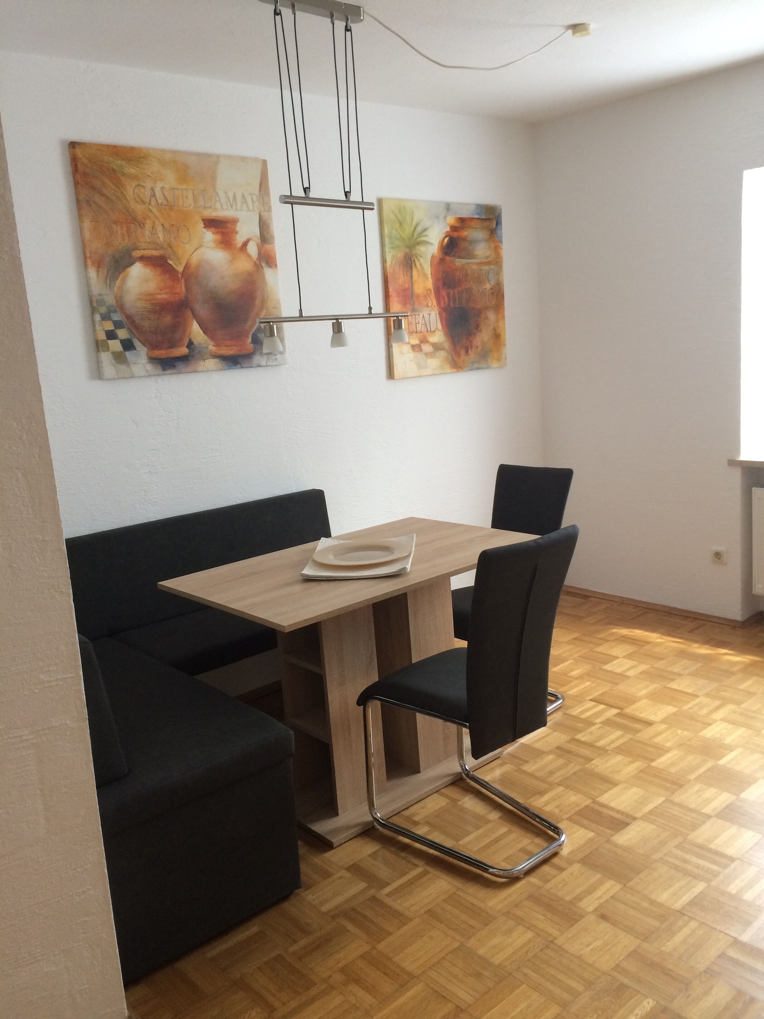 A dining area with a wooden table and black chairs, two paintings on the wall, and a checkered floor.