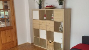 A living room with a wooden floor, a white coffee table with red candles, a grey sofa, and a wooden cabinet with plants. - Ferienwohnung im Grünen (Illschwang)