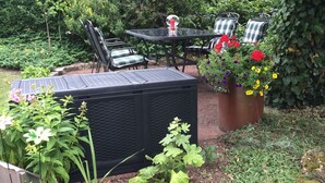 An outdoor patio with a table and chairs, surrounded by lush greenery and flowering plants. - Ferienwohnung im Grünen (Illschwang)