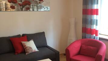 A living room with a dark grey sofa, a white coffee table, a red armchair, and a painting of red flowers on the wall.