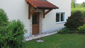 A house with a brown door, a small porch with a tiled roof, and a window with white shutters. - Ferienwohnung im Grünen (Illschwang)