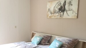 A bedroom with a bed, pillows, a painting of horses, and a wooden nightstand. - Ferienwohnung im Grünen (Illschwang)