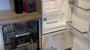 Ett kompakt kök med en inbyggd diskmaskin, en brödrost och ett kylskåp med glasdörr.