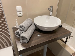 A bathroom with a large white sink, a towel dispenser, and a power outlet on the wall.