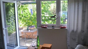 Une pièce dotée d’une porte-fenêtre coulissante donnant sur une terrasse, d’une petite table avec une bouteille et des verres, et d’une fenêtre décorée avec un motif de papillon.