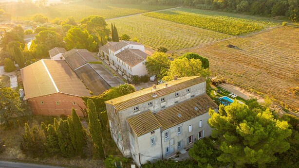 Vista aerea di una tenuta vinicola con diversi edifici, tra cui una grande casa con tetto in tegole e una struttura più piccola adiacente.