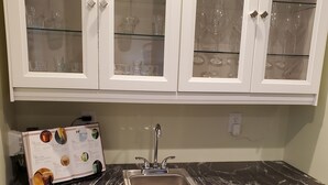 Een keuken met witte kastjes, een marmeren aanrechtblad, een ingebouwde vaatwasser en een kast voor wijnglazen.