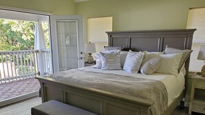 Een slaapkamer met een groot bed, een bankje, een nachtkastje en uitzicht op het groen.