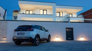 A modern two-story house with a white exterior, a driveway, and a parked white SUV.