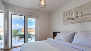 A bedroom with a large bed, a painting of sailboats, and a view through the glass door to an outdoor seating area.
