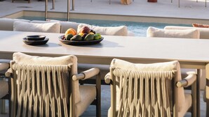 Un'area esterna con posti a sedere, una piscina, sedie e un tavolo con una ciotola di frutta.