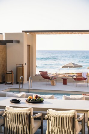 Un área de estar al aire libre con piscina, sillas y una mesa con frutero.