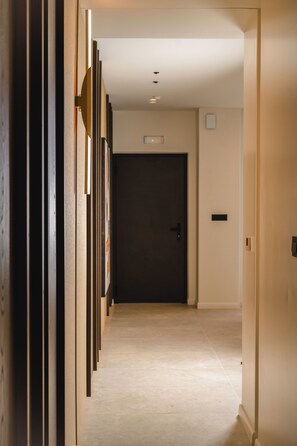 A hallway with a dark door at the end, light-colored walls, and a tiled floor.