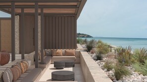 Ein moderner Außenbereich mit Sitzgelegenheiten, einer Steinsäule, einer Holzpergola und Blick aufs Meer.