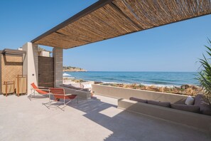 A modern outdoor seating area with a view of the sea, featuring a pergola, lounge chairs, and a sofa.