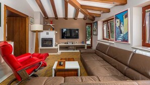 Un salon avec un fauteuil rouge, un canapé marron, des poutres en bois au plafond, un téléviseur et une cheminée.