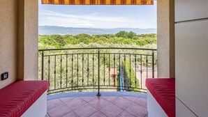 Un balcon doté d’une balustrade en métal, de sièges rembourrés de couleur rouge et offrant une vue sur un paysage verdoyant avec des montagnes au loin.