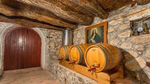 Une cave aux murs de pierre, avec des barils en bois, une porte en bois et un portrait accroché au mur.