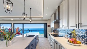 A modern kitchen with a large island, a view of the ocean, and a tropical-themed backsplash.
