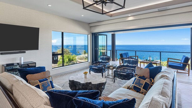 A modern living room with a large TV, comfortable seating, and a view of the ocean.