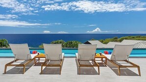 A poolside area with lounge chairs and a view of the ocean.