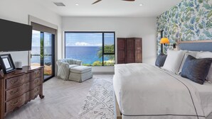 A bedroom with a large bed, a TV, a wooden dresser, and a view of the ocean.