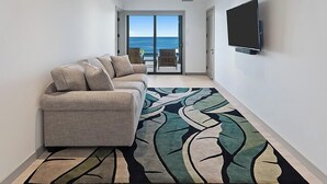 A modern living room with a sofa, a patterned rug, and a TV mounted on the wall.