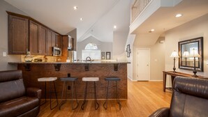 A spacious kitchen with wooden cabinets, a central island with stools, and a dining area with leather chairs. - Luxury Golf Condo with Beautiful Course View from Sunroom (Branson)