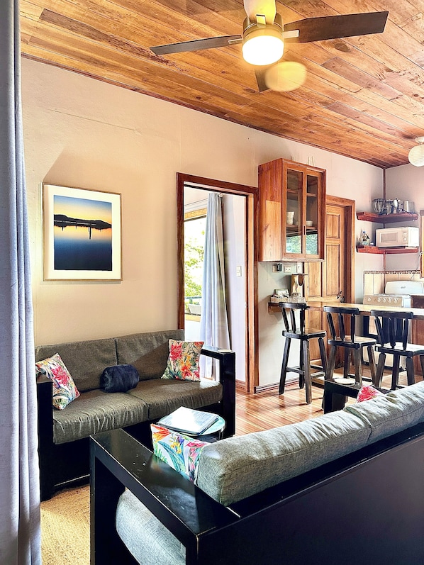 A living area with a sofa, a coffee table, a ceiling fan, and a kitchen area with a microwave and cabinets.