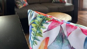 A living room with a sofa, colorful pillows, a framed picture on the wall, and a window.