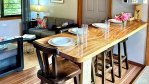 A dining area with a wooden table, chairs, a ceiling fan, a sofa, a lamp, and a window with curtains.