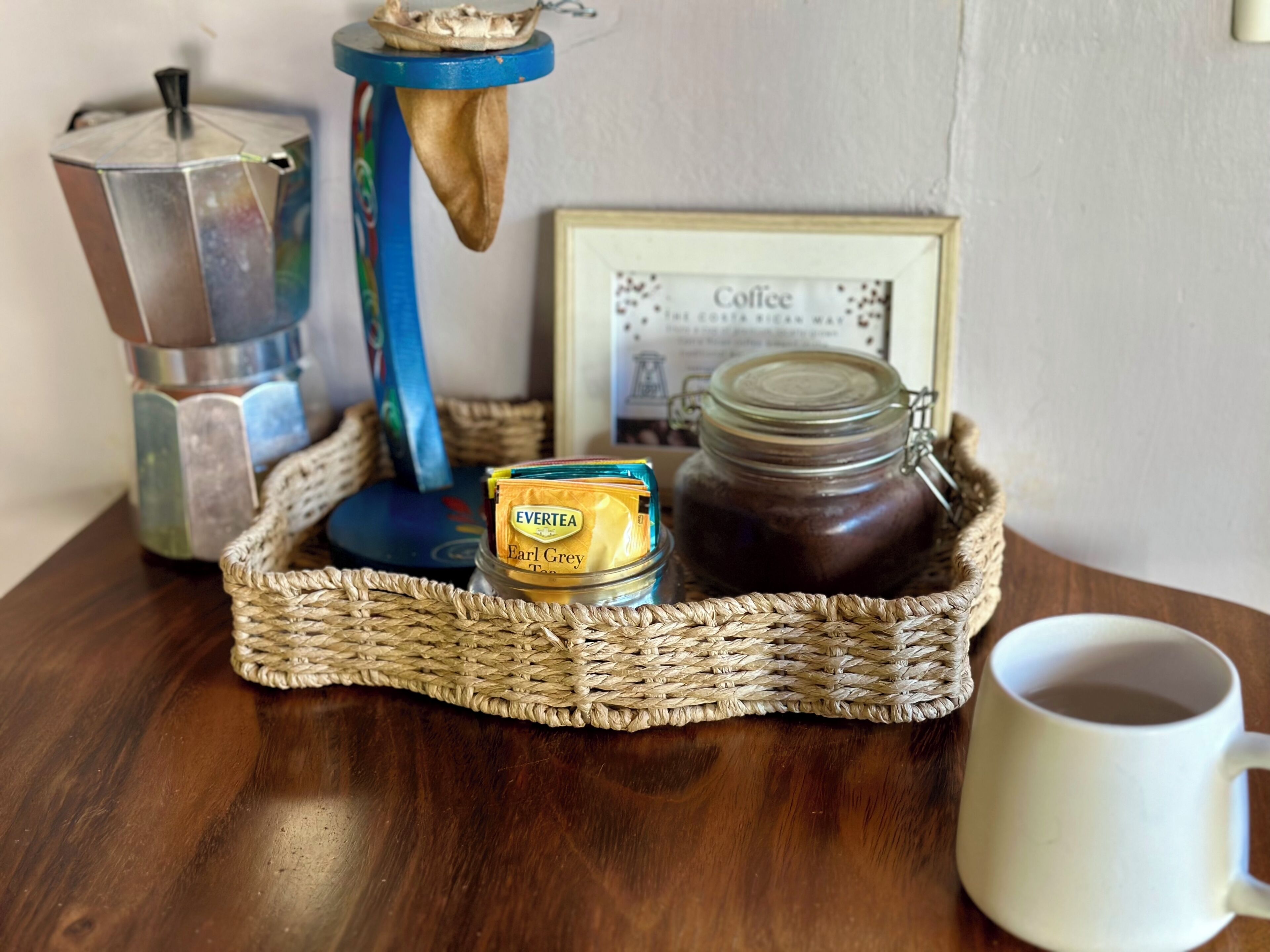 En kaffemaskine, et glas Earl Grey te, en kop og et indramet certifikat på et træbord.