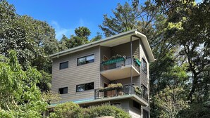 A multi-story building with balconies, surrounded by lush greenery and trees.