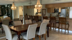 Un comedor amplio con una gran mesa de madera y sillas a juego, un candelabro y una cocina al fondo.