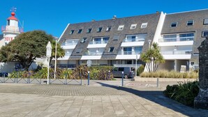 Un edificio moderno con facciata in pietra, un faro con tetto rosso e un viale lastricato con vegetazione.