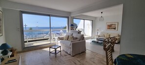 A spacious living room with a large sliding glass door leading to a balcony, a sofa, a coffee table, and a chair.