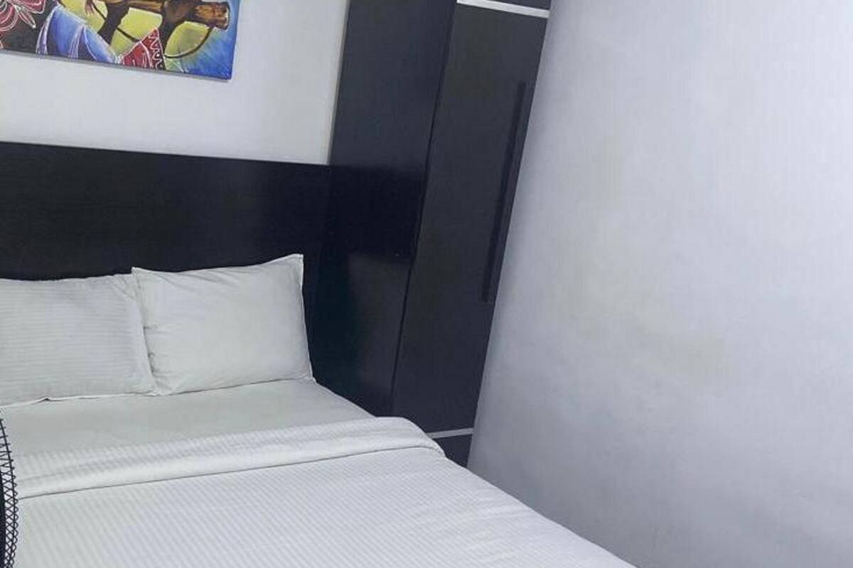 Un dormitorio con una cama, un armario negro y un cuadro en la pared.