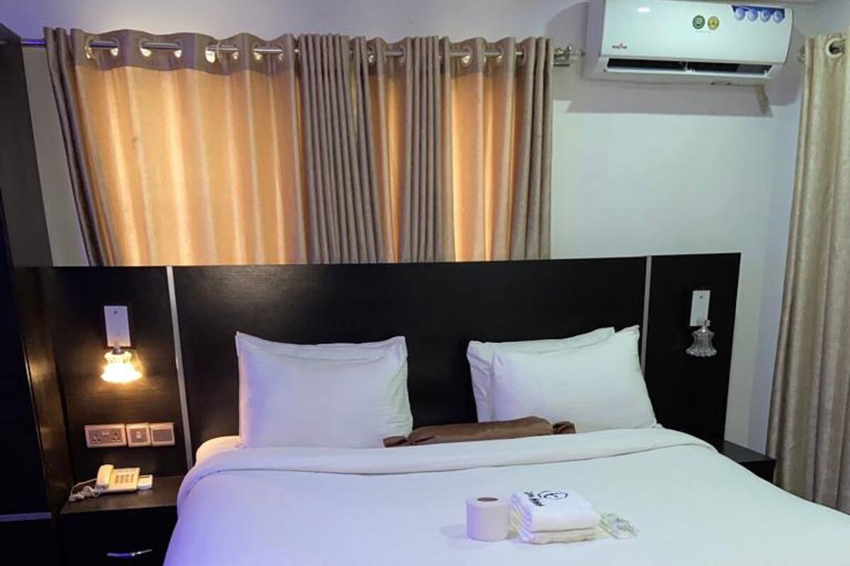 Una habitación de hotel con una cama grande, una mesita de noche con lámpara y un equipo de aire acondicionado en la pared.