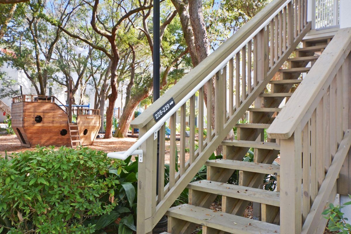 A wooden staircase with a handrail, surrounded by greenery and trees.