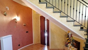 A spacious hallway with a tiled floor, a radiator, a staircase with black balusters, and a flower arrangement. - Villa Rosetta in the middle of nature, surrounded by palm and olive trees  (Pizzo)