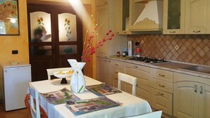 A kitchen with a dining table set for two, a refrigerator, and cabinets. - Villa Rosetta in the middle of nature, surrounded by palm and olive trees  (Pizzo)